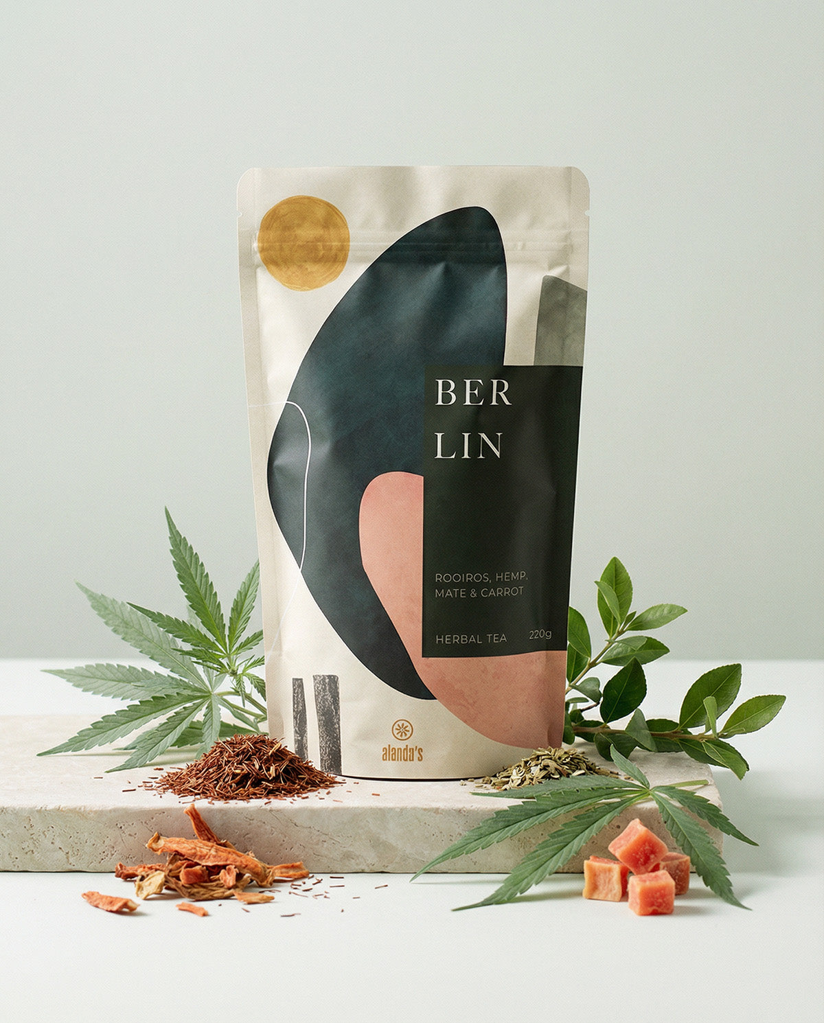 Alanda's Tea BERLIN Doypack Produktfoto mit Hanfpflanze, Rooibos, Karotte und Mate auf Steinpodest