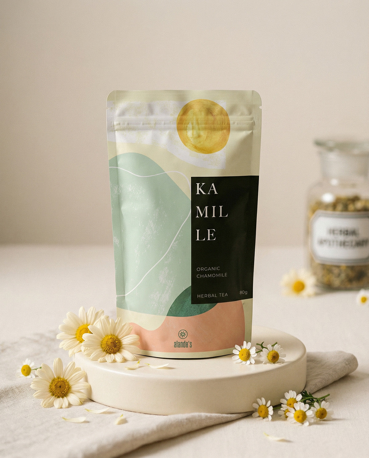 KAMILLE Organic Chamomile Kräutertee von Alandas – Doypack auf Podest mit frischen Kamillenblüten und Glasgefäß