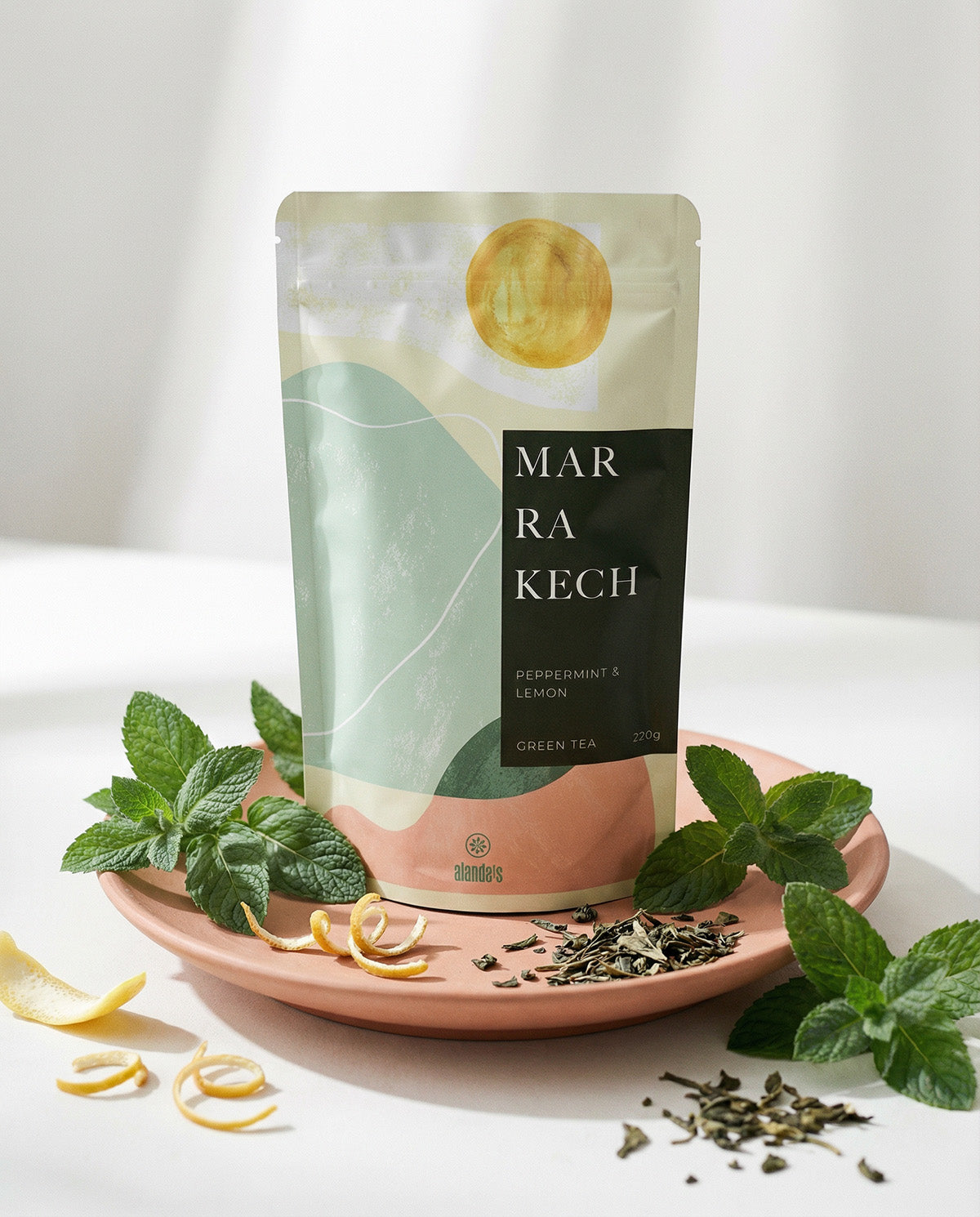 Alanda's Tea MARRAKECH Grüntee Doypack auf Rosa Teller mit frischer Minze und Zitronenschale – Premium Tee kaufen