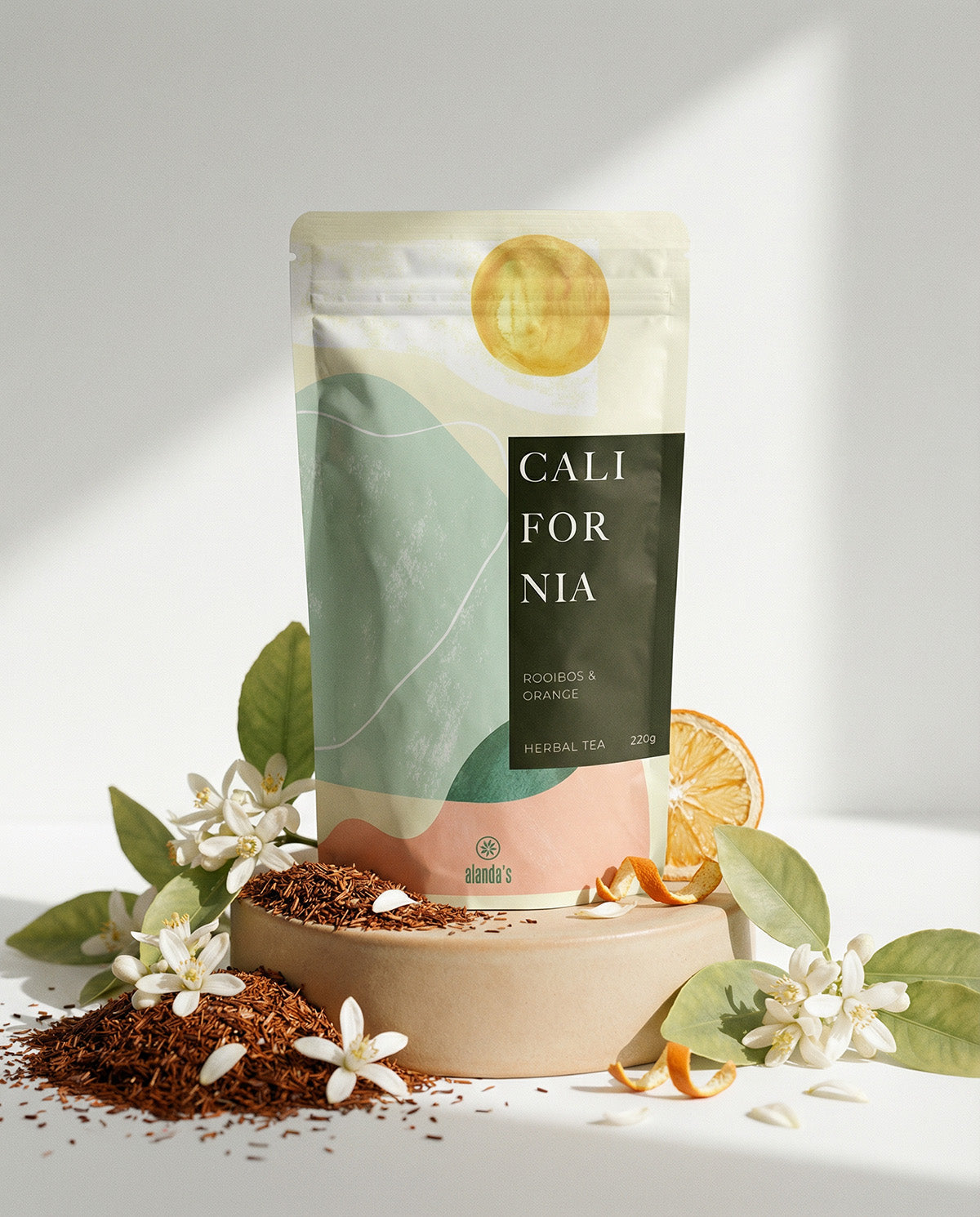 CALIFORNIA Rooibos & Orange Tee von Alandas – elegante Verpackung mit frischen Orangen und Blüten auf Podest