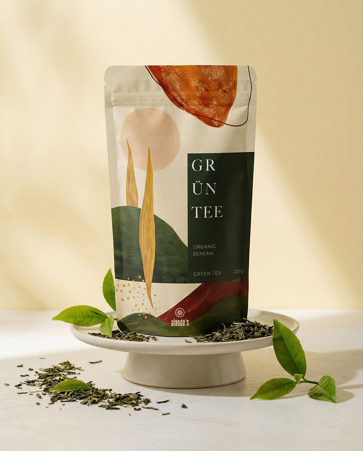 GRÜNTEE Organic Sencha von Alandas – elegante Verpackung mit frischen grünen Teeblättern auf Podest