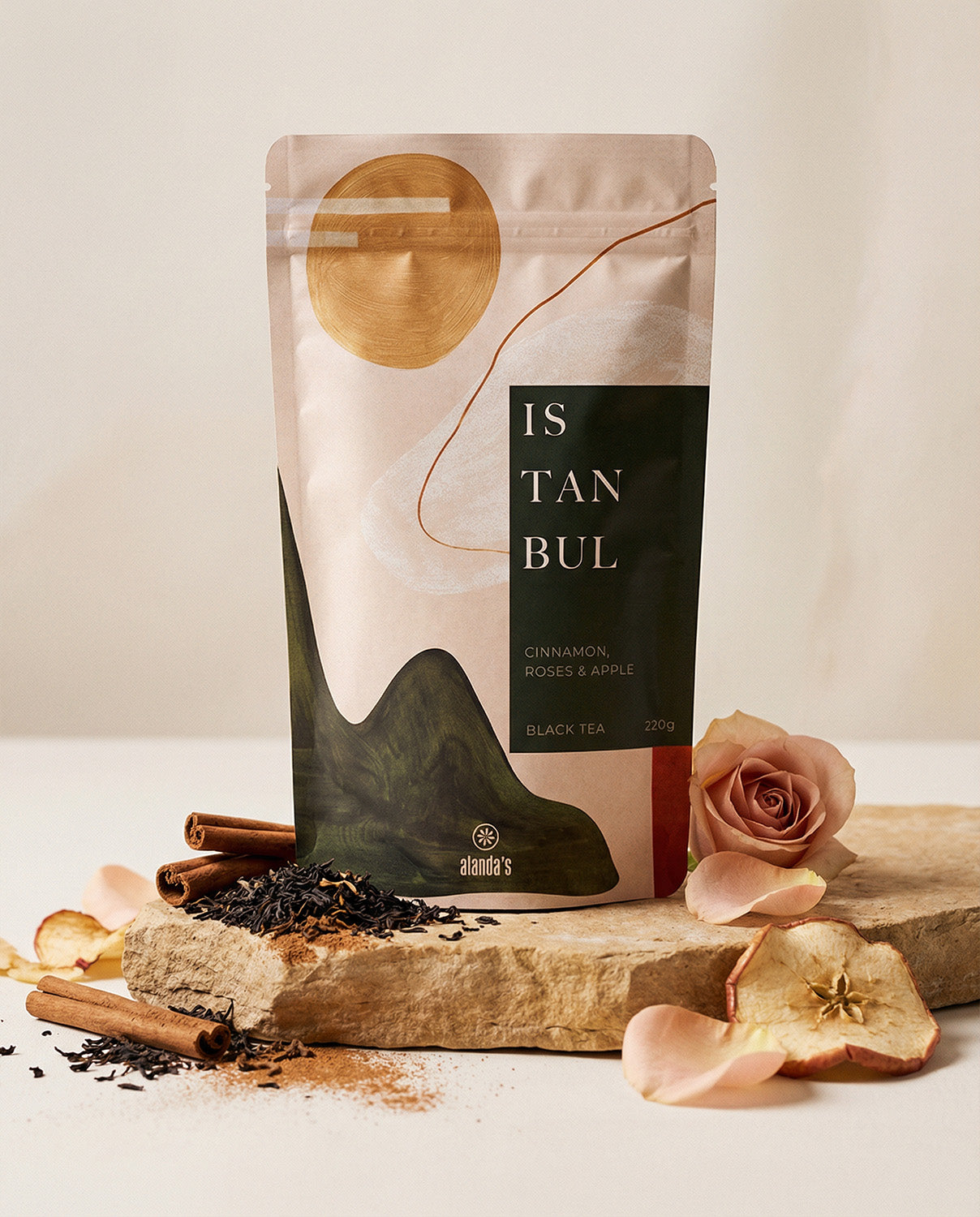 Alanda's Tea ISTANBUL Doypack Produktfoto mit Zimtstängen, Apfelscheiben und Rose auf Steinpodest