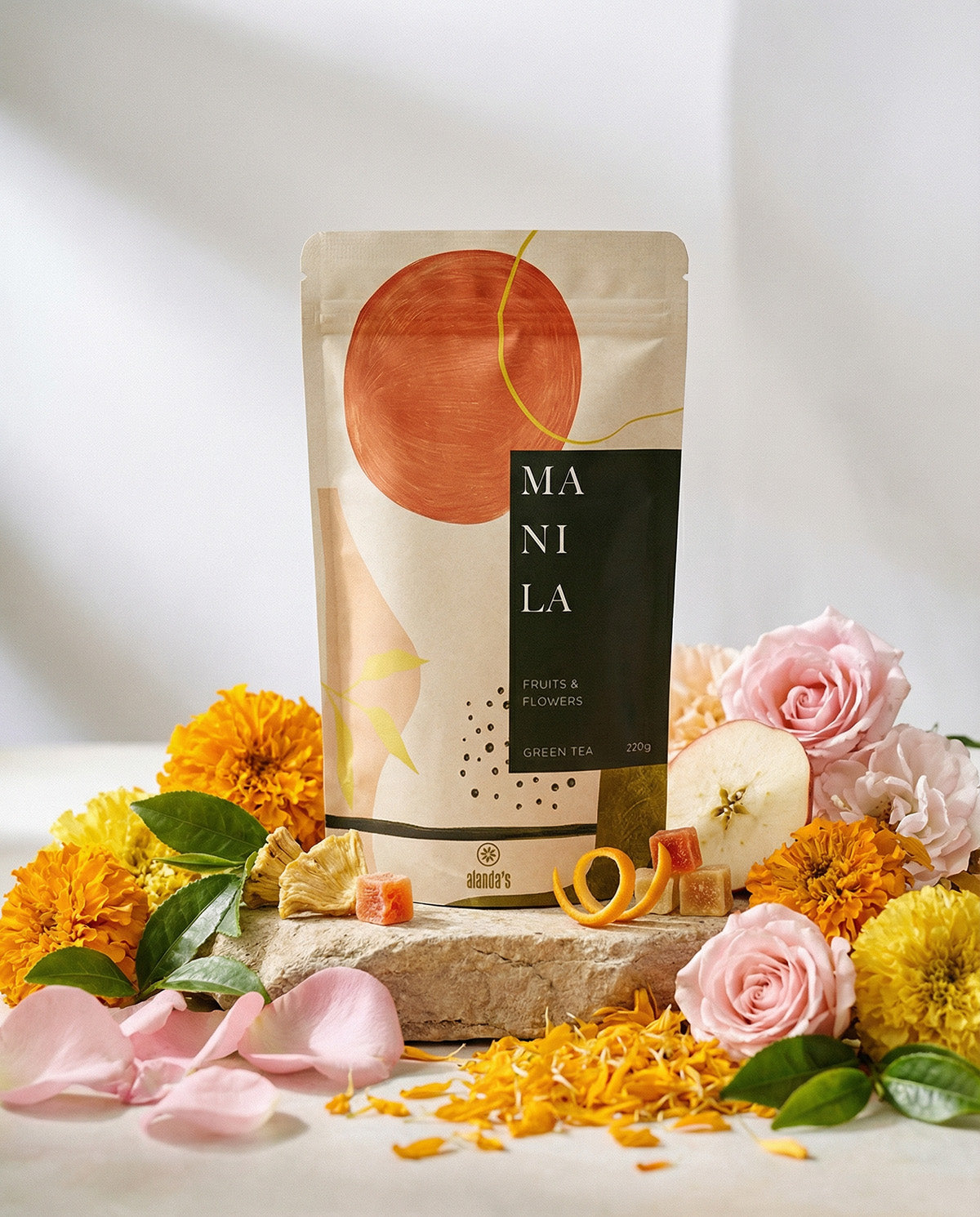 Alanda's Tea MANILA Doypack Produktfoto mit Rosen, Ringelblumen, Apfel und Ananas auf Steinpodest