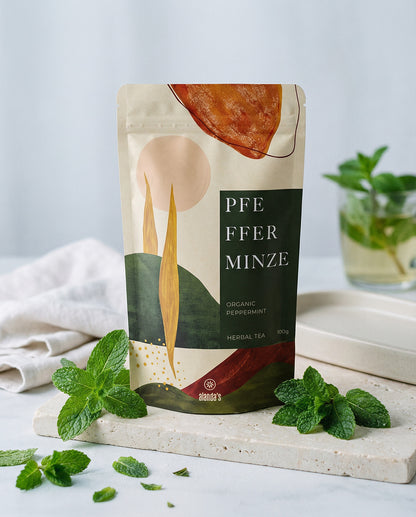 PFEFFERMINZE Organic Peppermint Kräutertee von Alandas – Doypack auf Steinpodest mit frischen Minzblättern und Teetasse