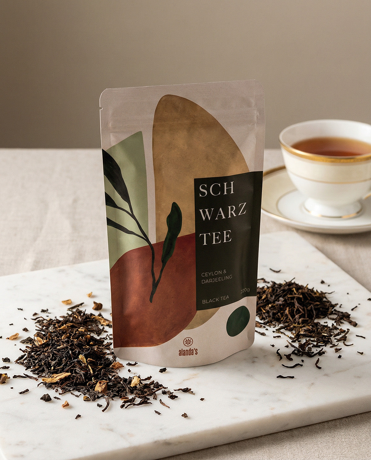 SCHWARZTEE Ceylon & Darjeeling von Alandas – Doypack mit losem schwarzen Tee und Teetasse auf Marmorfläche